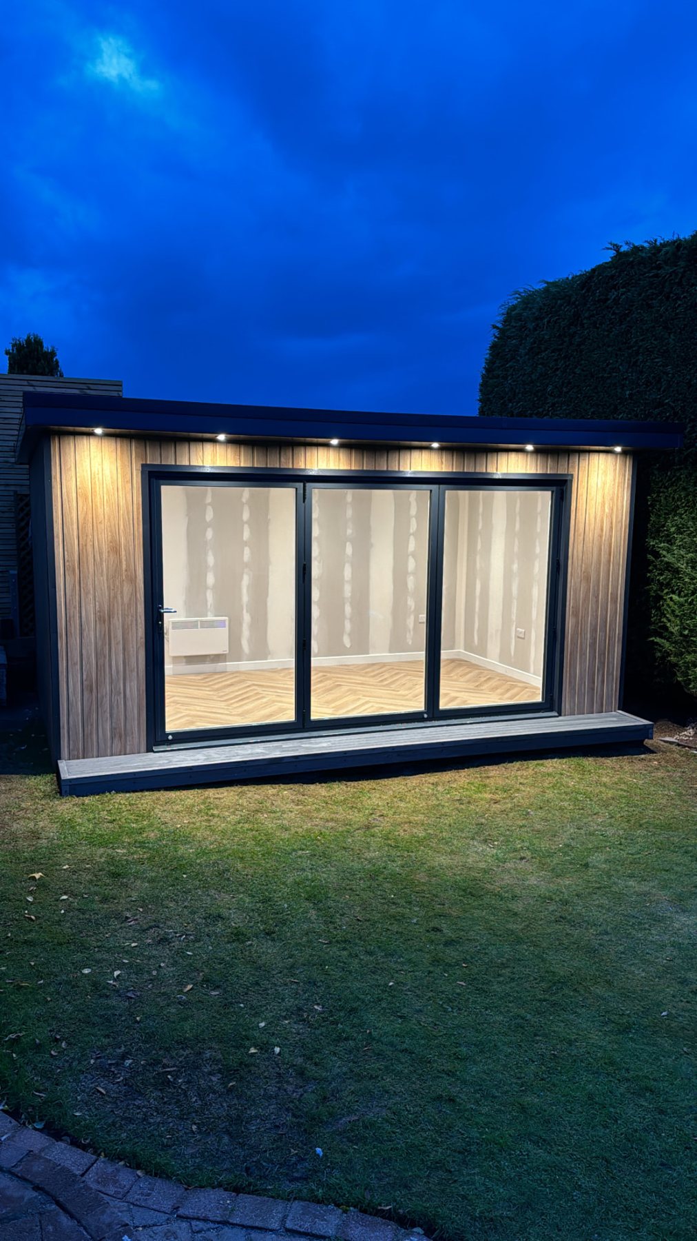 Illuminated garden room with vertical cladding and large sliding glass doors at dusk | Signature Garden Rooms, Central Scotland