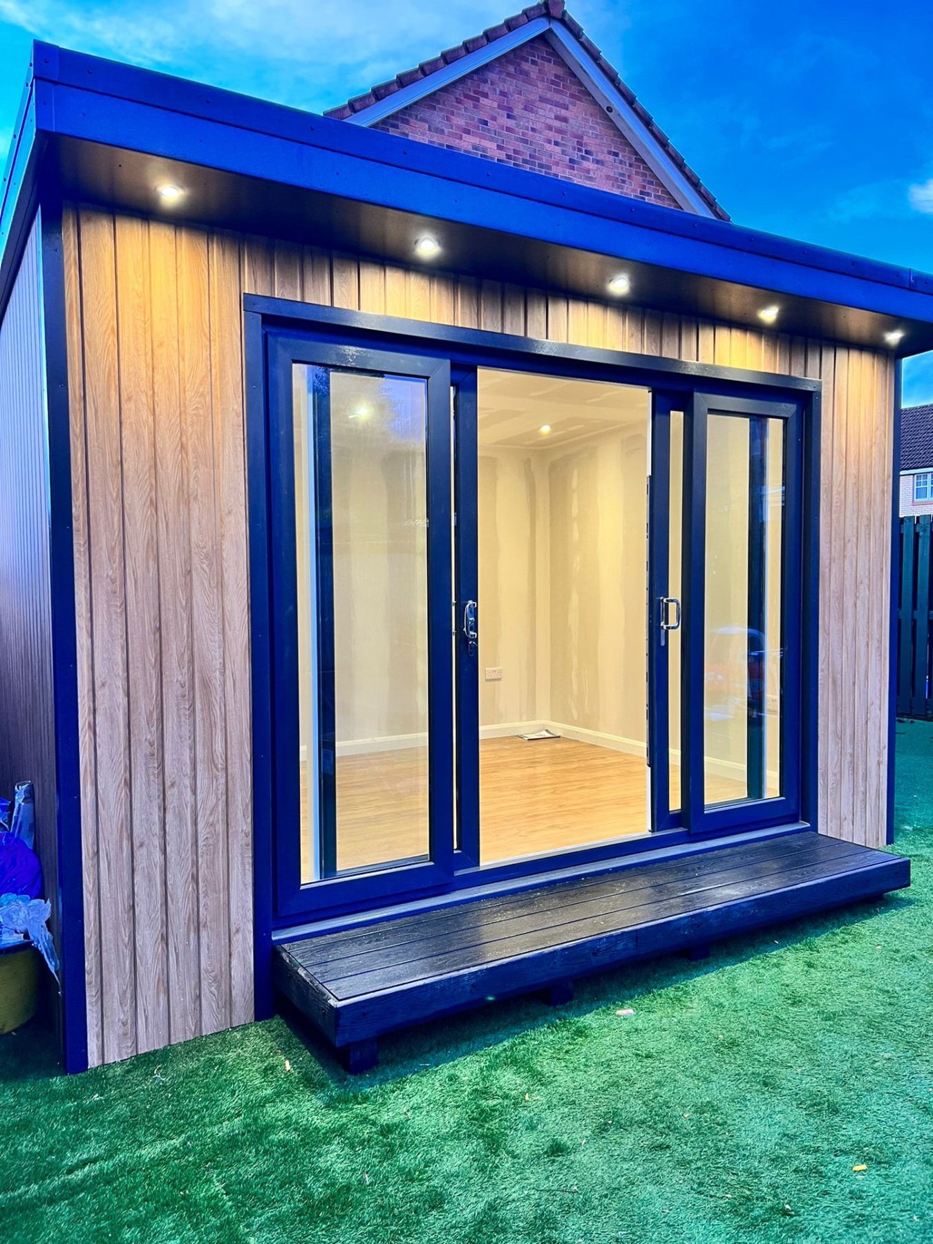 Modern timber clad garden room with dark sliding glass doors and soffit spotlights | Signature Garden Rooms, Central Scotland