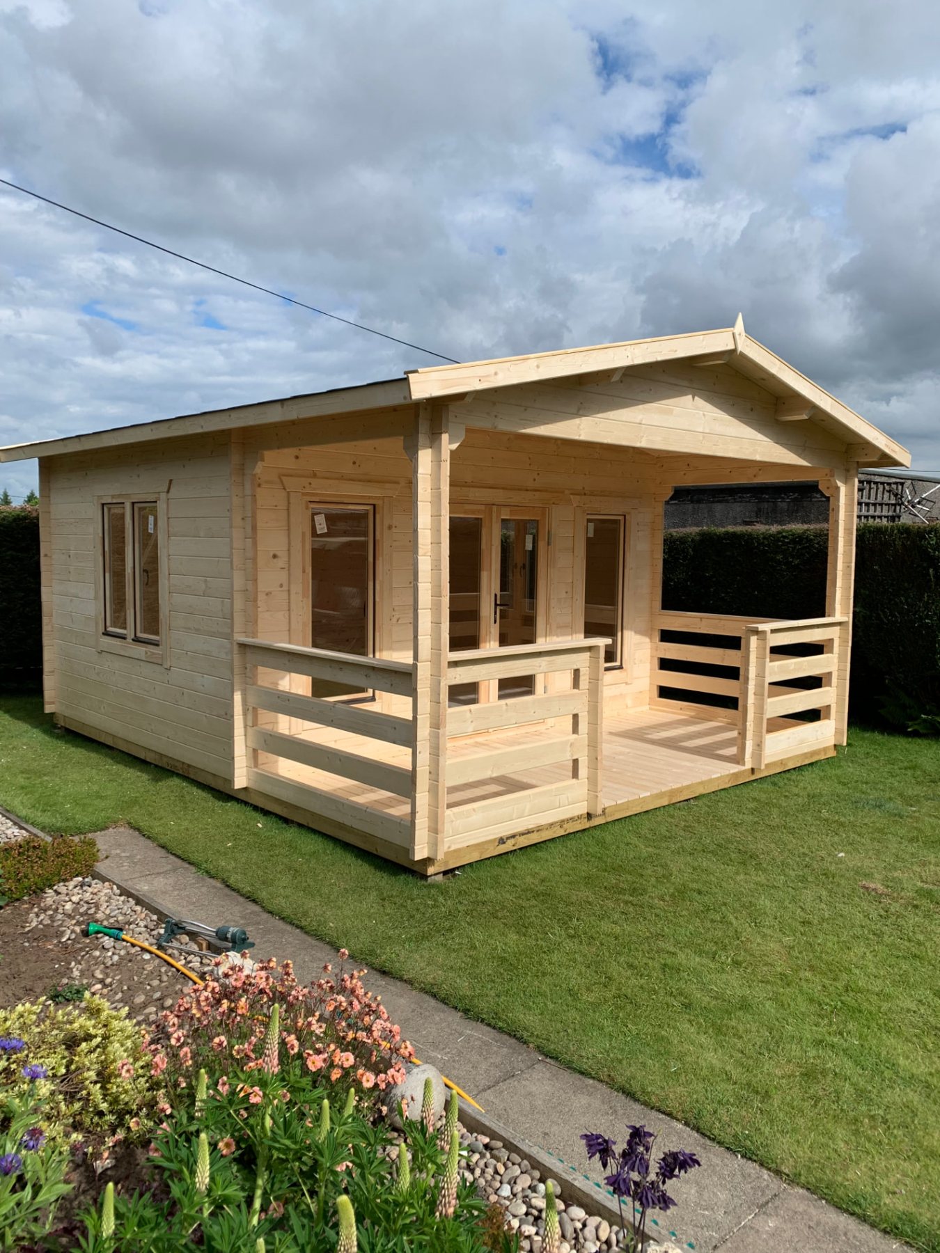 A large timber log cabin featuring an integrated front veranda on a lawn | Signature Garden Rooms, Central Scotland