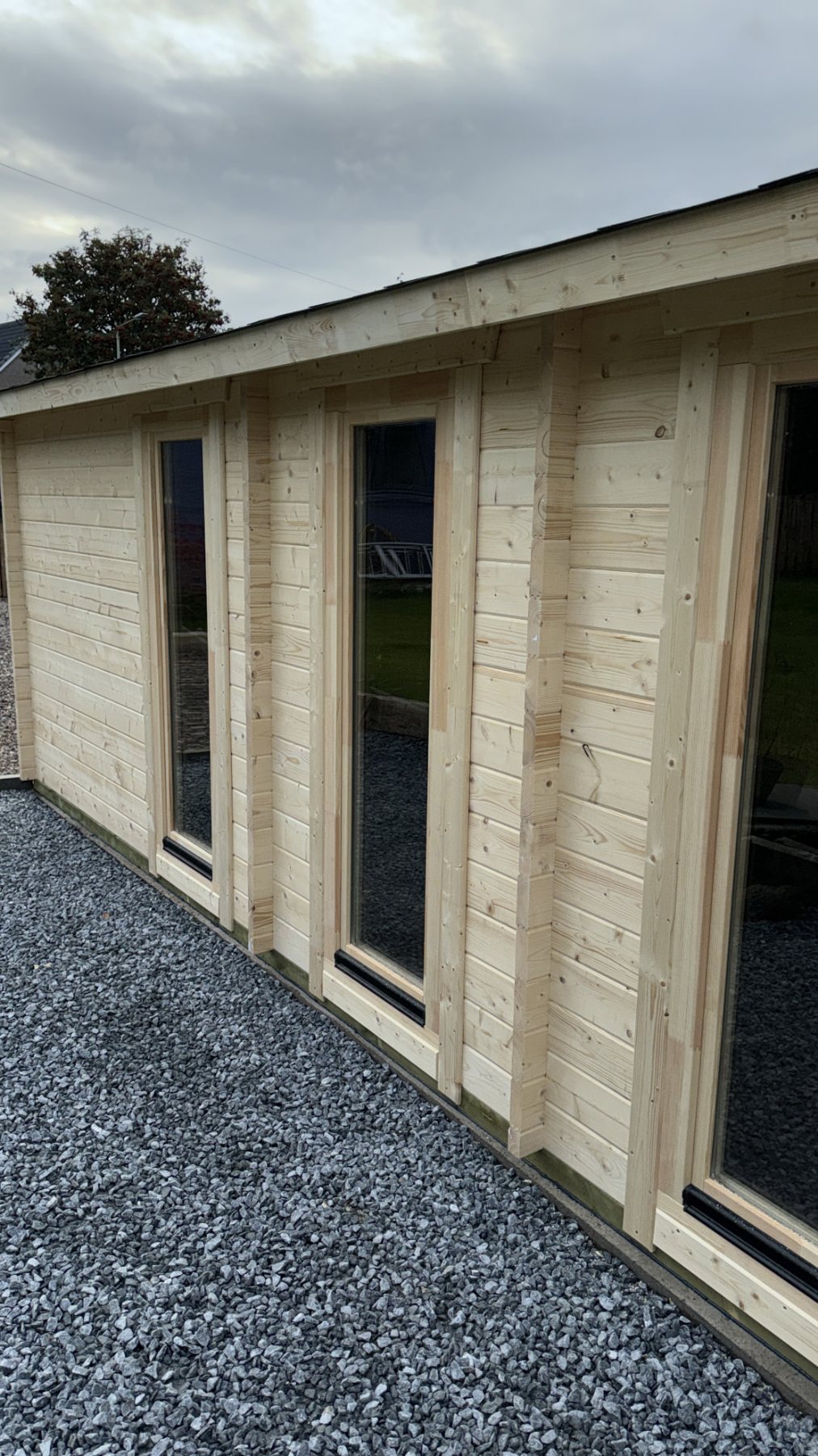 Exterior side view of an untreated timber log cabin with tall glass windows | Signature Garden Rooms, Central Scotland