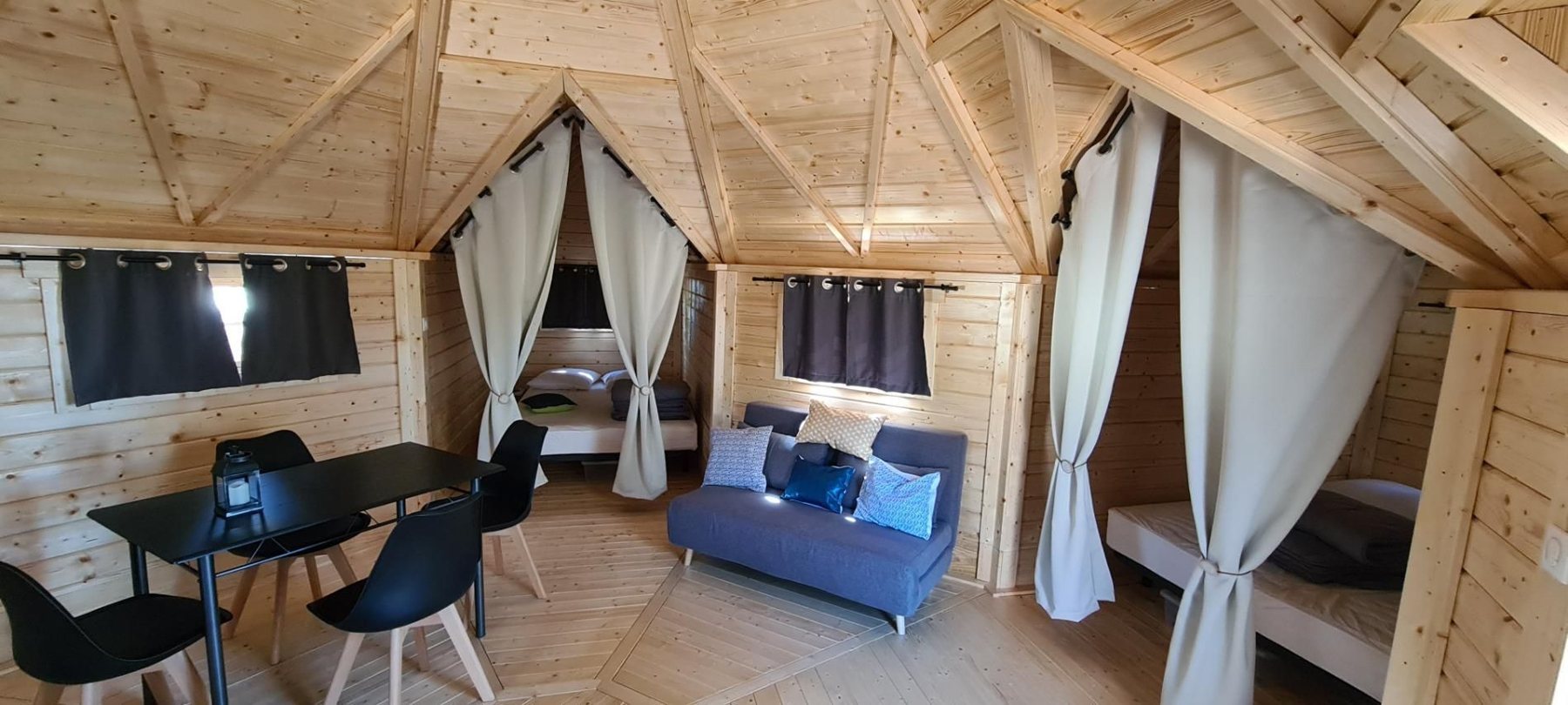 Interior of a wooden cabin featuring dining area, sofa, and curtained bed alcoves | Signature Garden Rooms, Central Scotland