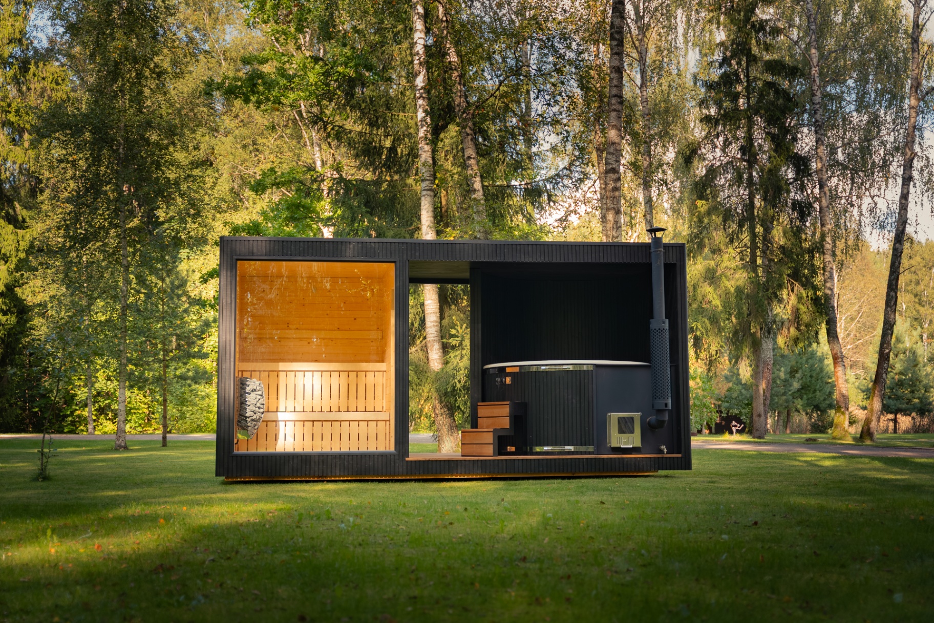 The same Tauras Grand Ebony sauna and hot tub in a sunlit birch grove, a Signature Garden Rooms installation photographed in high summer.