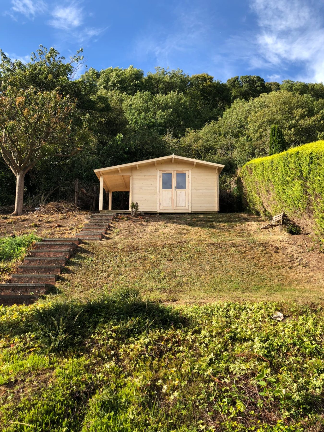 Light timber log cabin with side canopy situated atop a sloped lawn | Signature Garden Rooms, Central Scotland