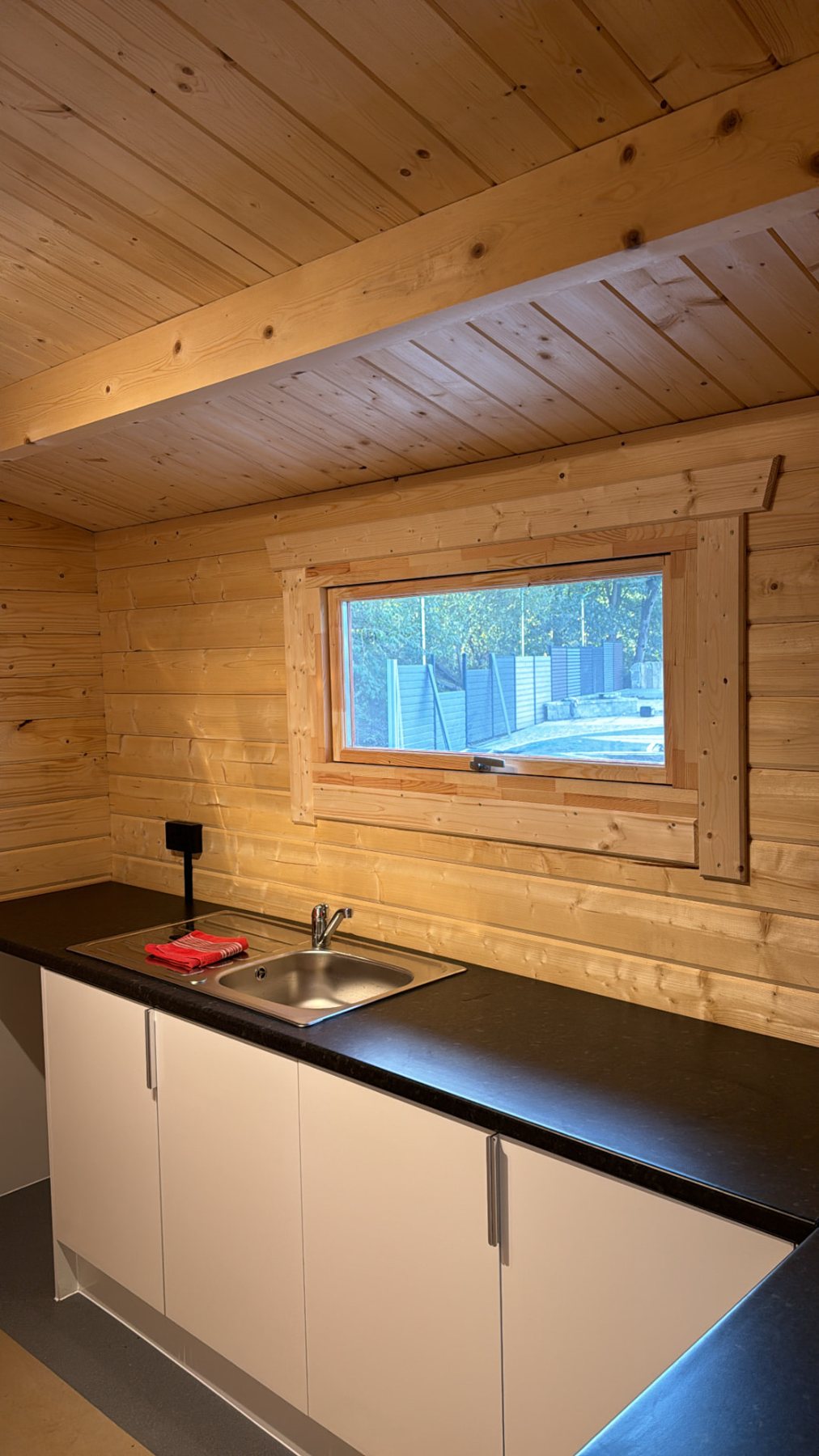 Interior of a timber cabin showing white kitchen cabinets, countertop, sink, and window | Signature Garden Rooms, Central Scotland