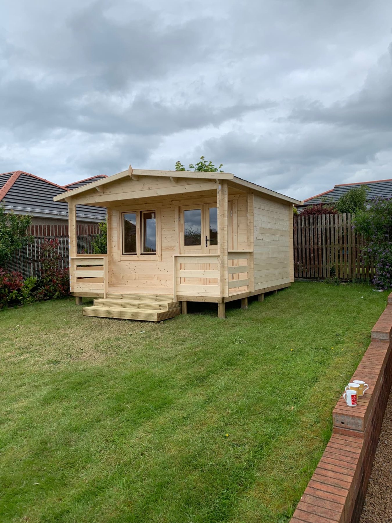 A timber log cabin with a covered porch set on a residential lawn | Signature Garden Rooms, Central Scotland