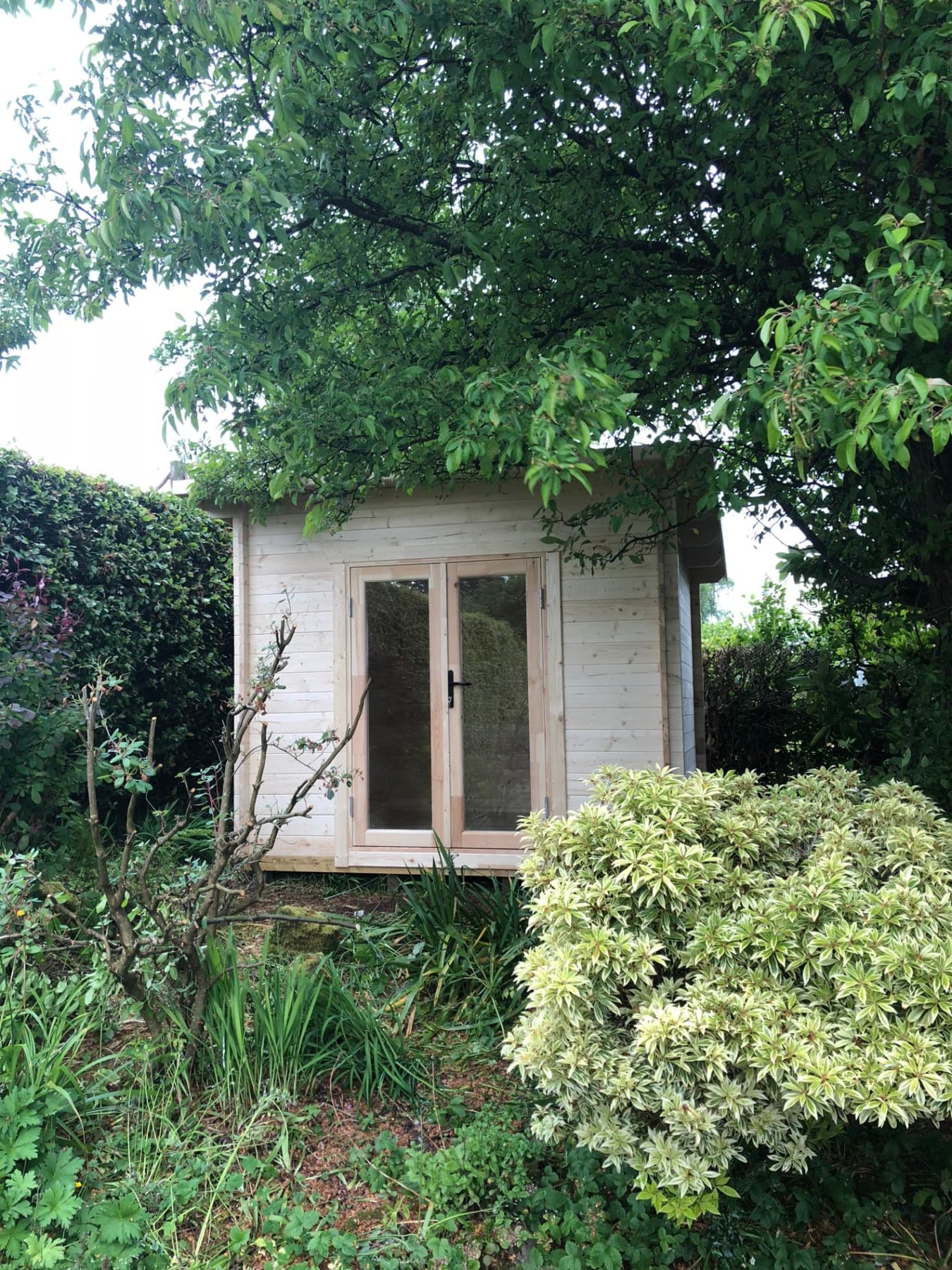 Small light wood log cabin with double glass doors nestled beneath leafy trees | Signature Garden Rooms, Central Scotland