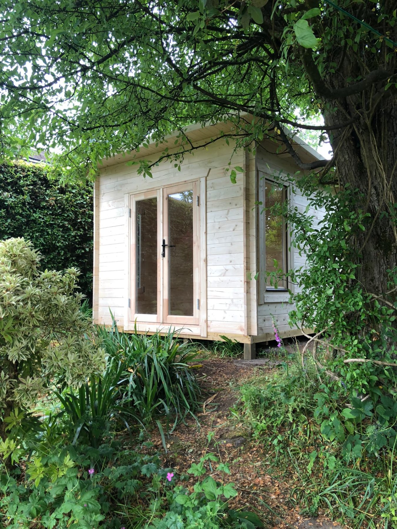 Small light timber log cabin with glass double doors surrounded by garden foliage | Signature Garden Rooms, Central Scotland