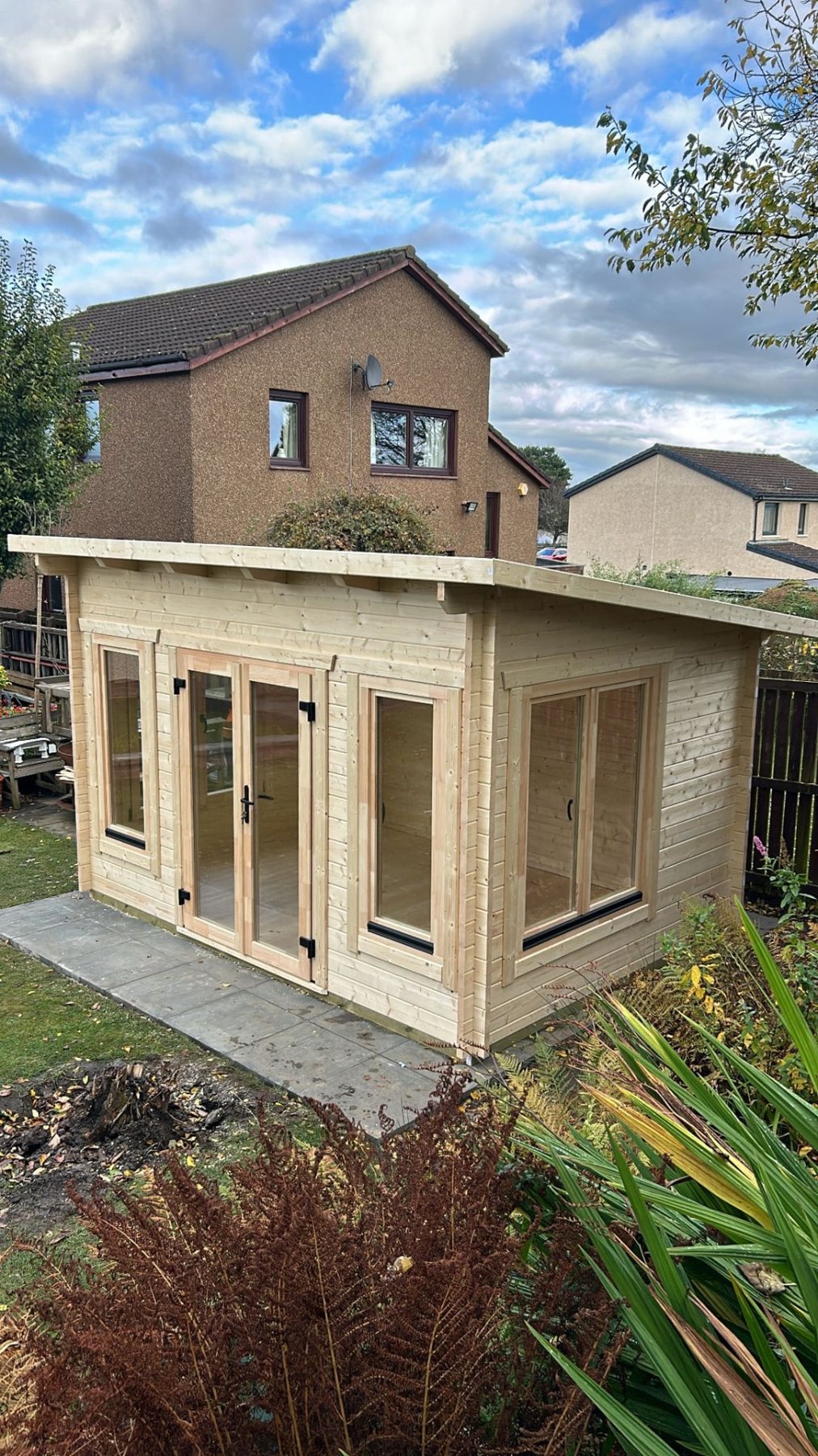 Unpainted wooden log cabin with pent roof and double glass doors in garden | Signature Garden Rooms, Central Scotland