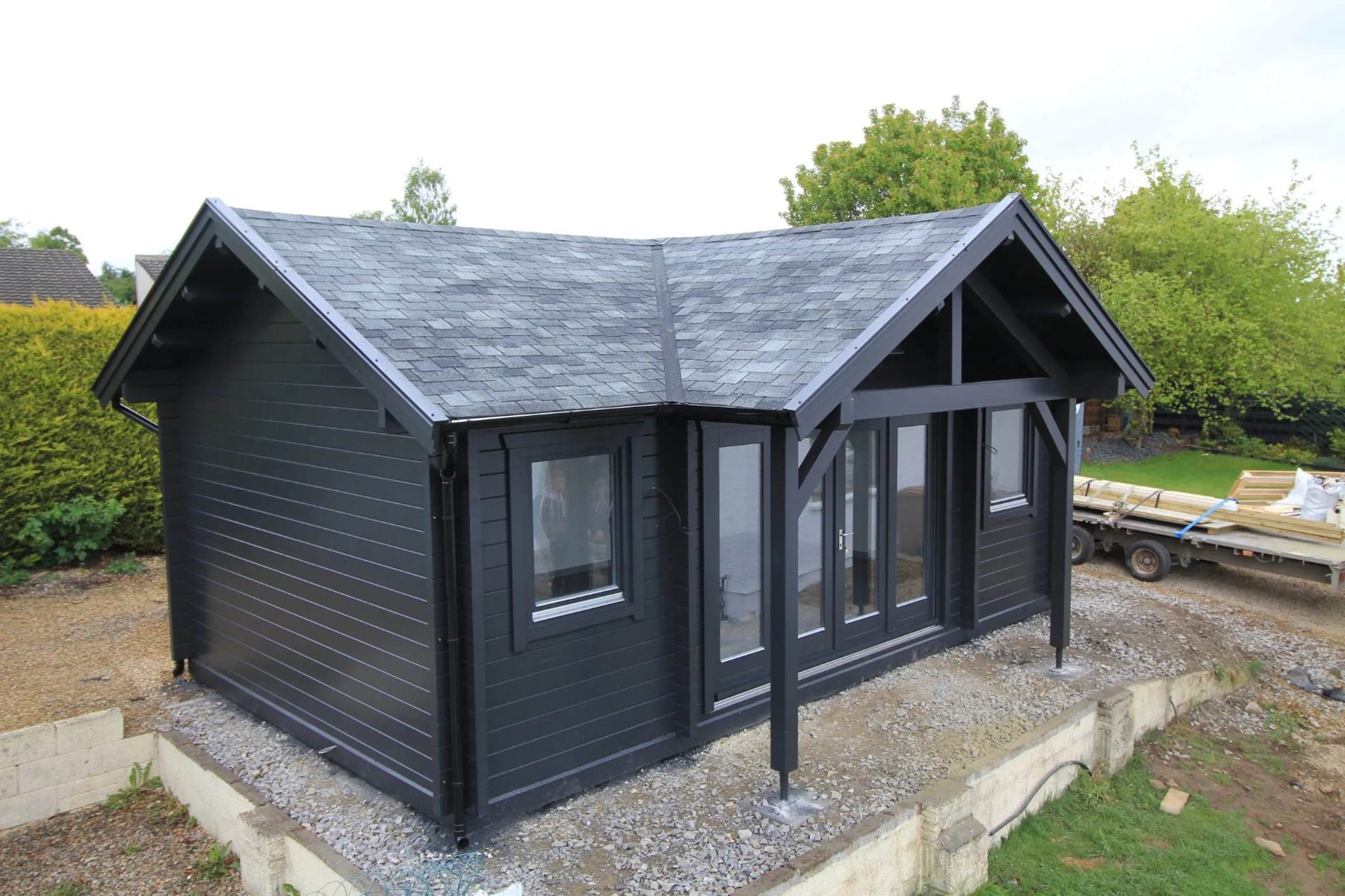 Dark grey painted L-shaped log cabin with apex shingle roof in garden | Signature Garden Rooms, Central Scotland