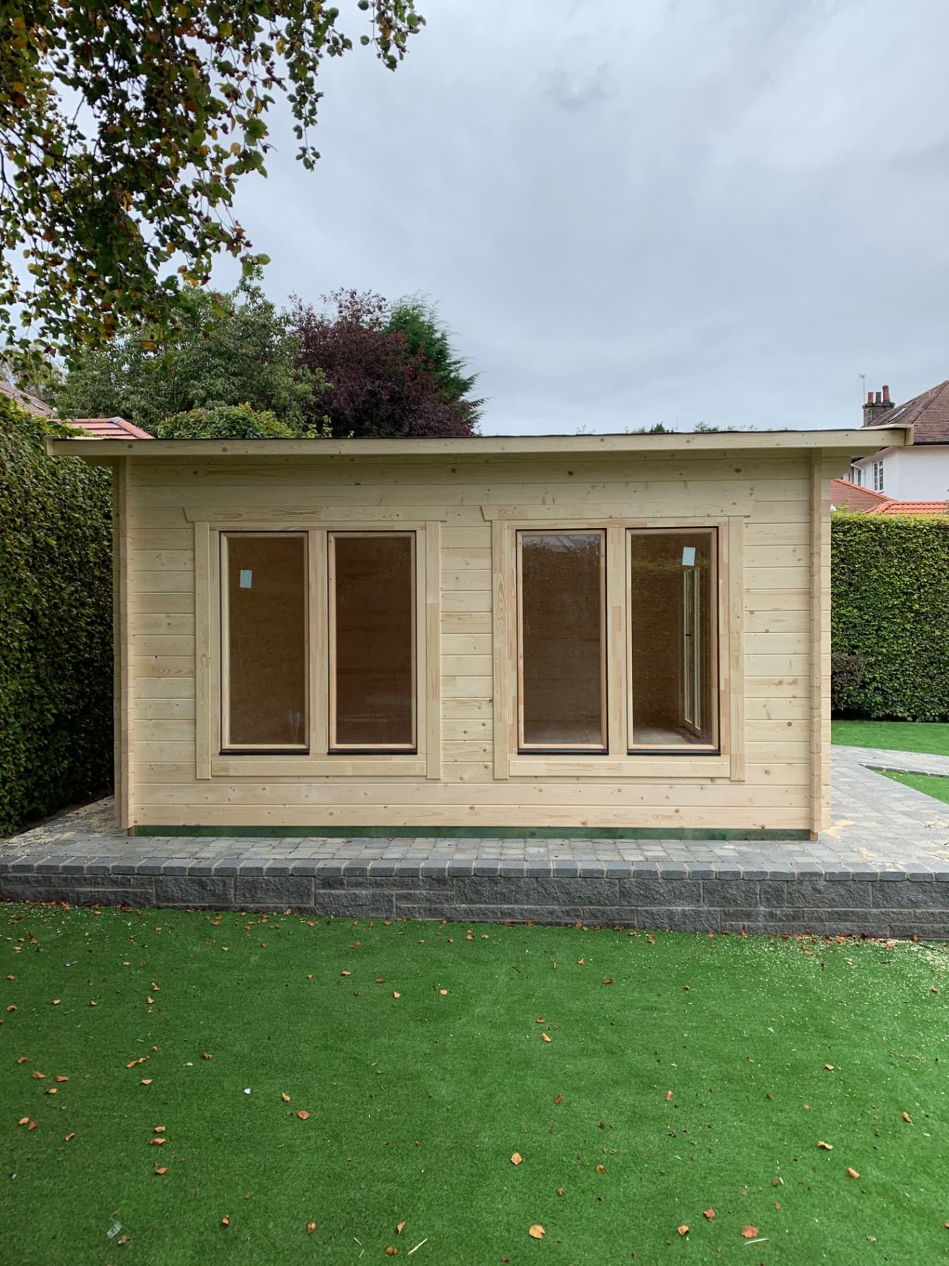 Front view of an unfinished light timber log cabin on a paved patio | Signature Garden Rooms, Central Scotland