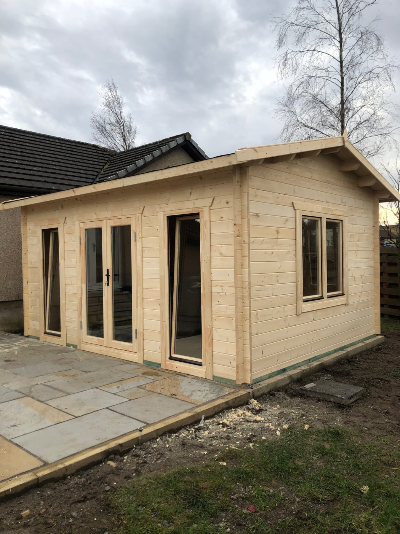 Light untreated timber log cabin with glass double doors installed on stone patio | Signature Garden Rooms, Central Scotland
