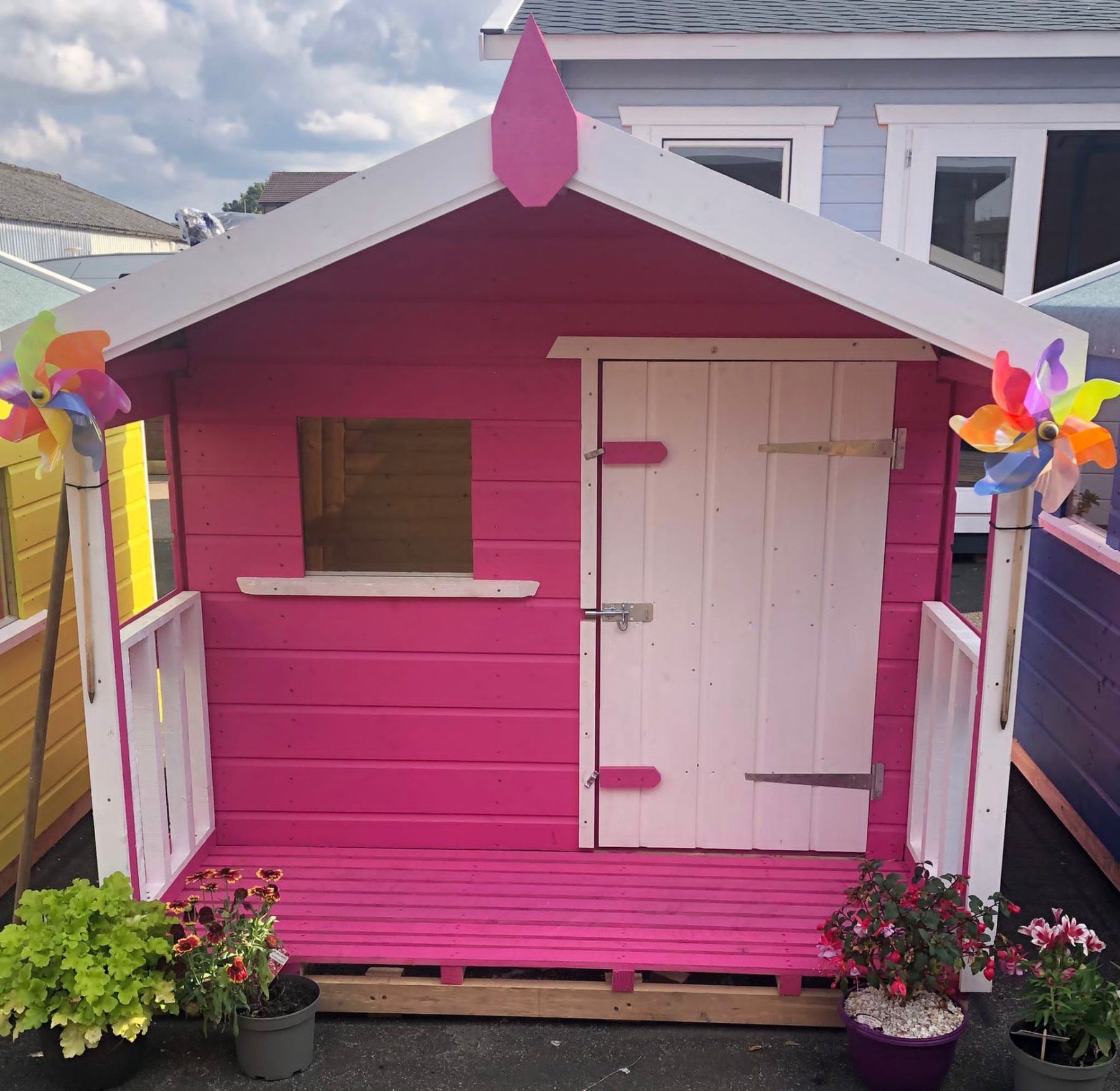 A pink and white wooden children's playhouse with veranda and decorative pinwheels outdoors | Signature Garden Rooms, Central Scotland