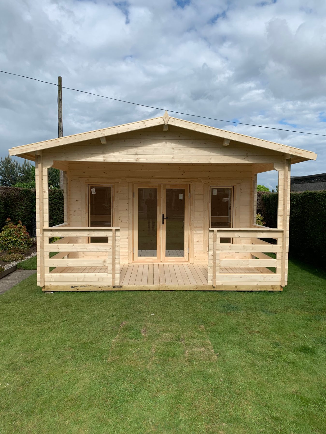 Light wood log cabin with apex roof and covered front veranda on green lawn | Signature Garden Rooms, Central Scotland