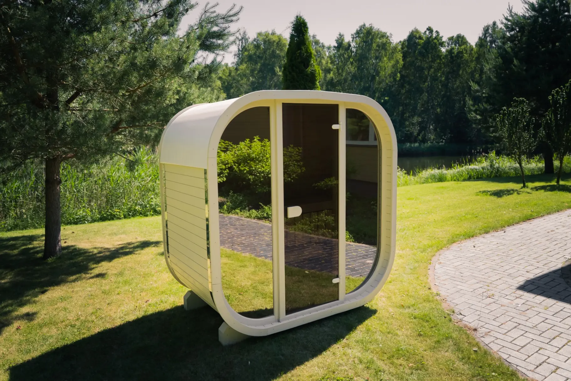 Beige curved-cube outdoor sauna beside a garden pond