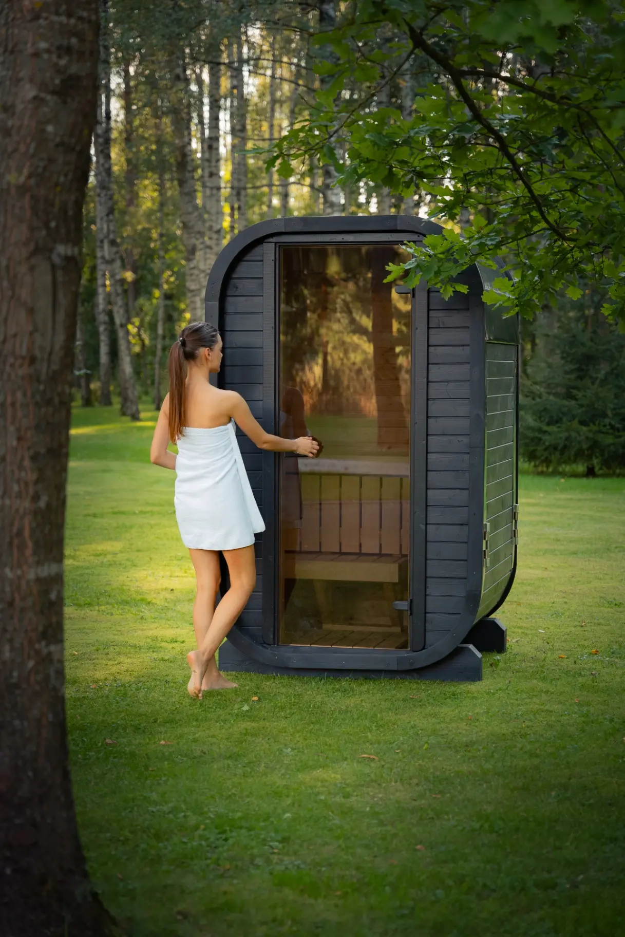 Ebony curved-cube sauna at sunset in a woodland garden